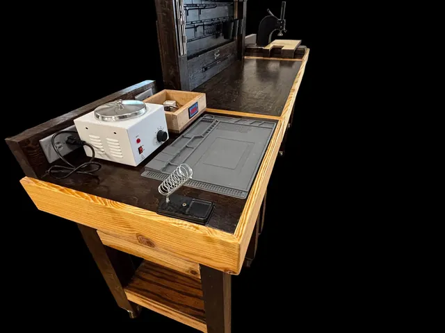 A workbench with a soldering mat and equipment, photographed against a black background.