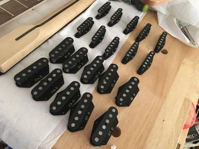 A pile of black single-coil pickups on a wooden workbench.
