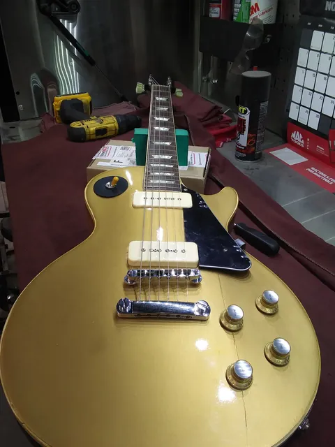 A gold-top single-cutaway guitar with two P-90 pickups lying on a workbench.