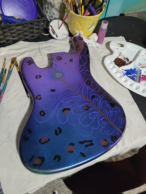 A guitar body with a swirling blue-to-purple painted finish, with paint supplies nearby.