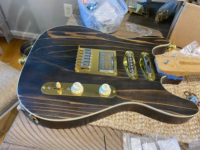 A guitar body in dark striped wood with gold hardware and white edge binding, being assembled.
