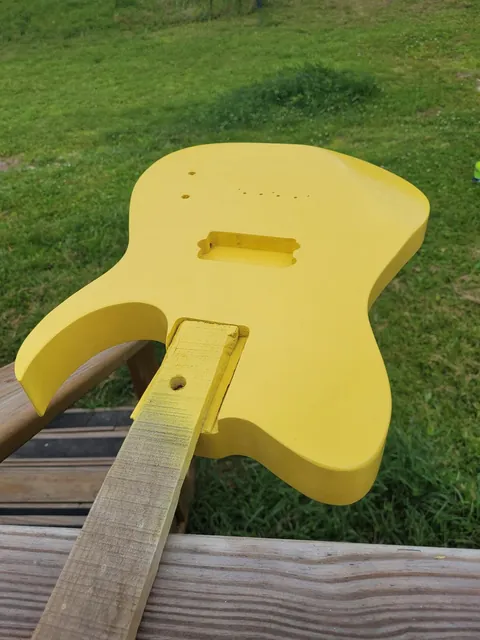 A freshly painted yellow guitar body and neck lying on the grass.