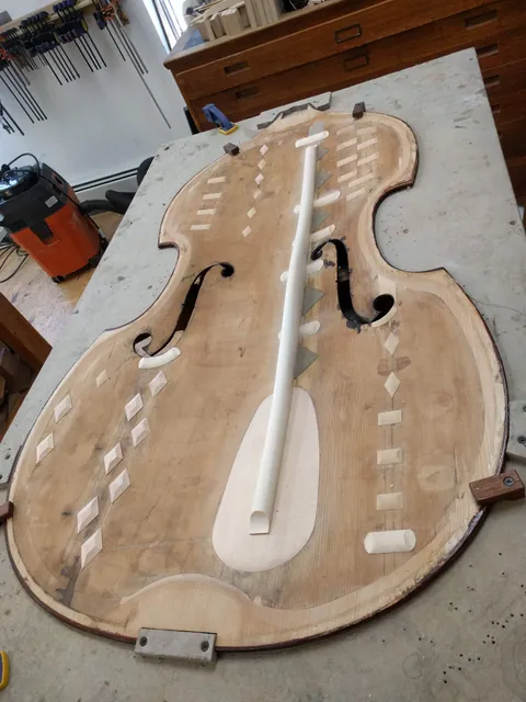 An unfinished archtop guitar top with f-holes and a white center brace on the workbench.